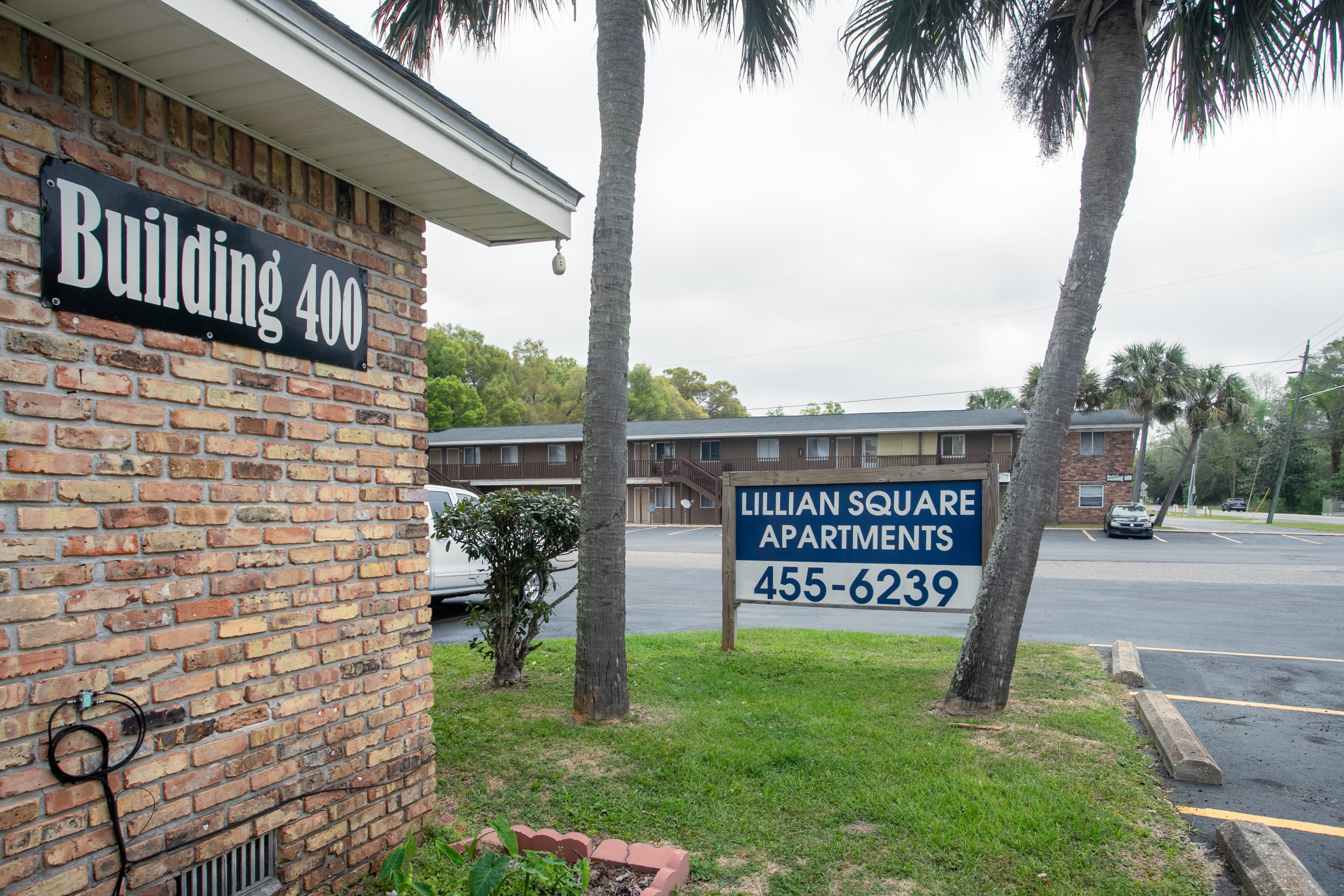 A sign for Lillian Square Apartments is displayed in front of a brick building.
